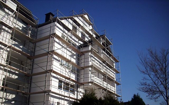 Weiß beschichtetes Mehrfamilienhaus mit Giebeln hinter einem Baugerüst vor tiefblauem Himmel