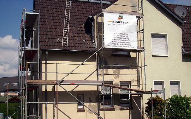 Wohnhaus mit teilweise abgeschlagenem Putz, Baugerüst mit Nemecsek-Bauschild
