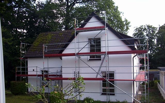 Weißes Einfamilienhaus mit Satteldach und Gerüst, umgeben von Bäumen