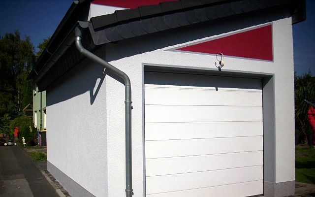 Garage mit hellem Reibeputz, grauem Sockel und weißem Sektionaltor