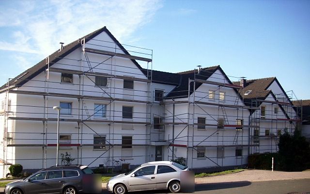 Reihe von Mehrfamilienhäusern mit Giebeln, alle mit Baugerüst, davor eine Straße