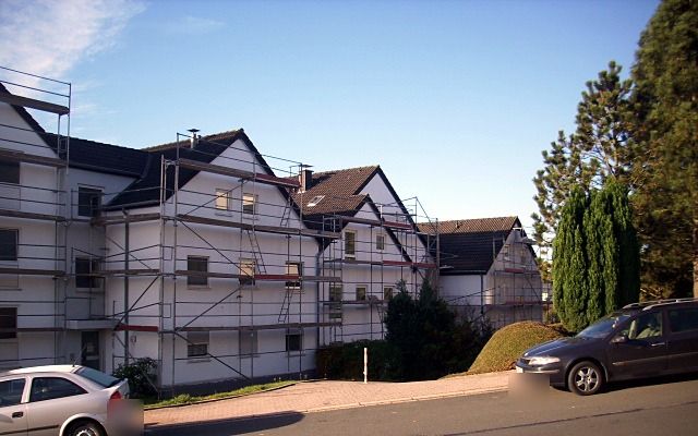 Eingerüstete Wohnanlage mit mehreren Giebeln, seitlich von der Straße aus gesehen
