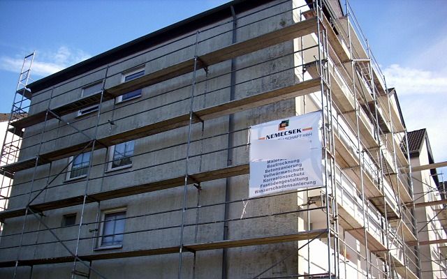 Mehrgeschossiges Wohnhaus mit verwitterter Fassade, davor ein Baugerüst mit Bauschild