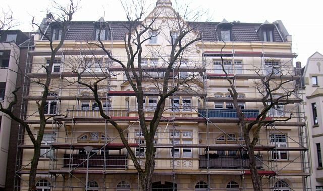Hoher Gründerzeit-Altbau mit Stuckfassade, vollständig eingerüstet, davor kahle Bäume