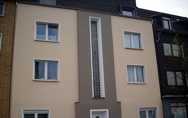 Dreigeschossiges Mehrfamilienhaus in Beige mit grauem Mittelteil und schmalem Glasbausteinfenster