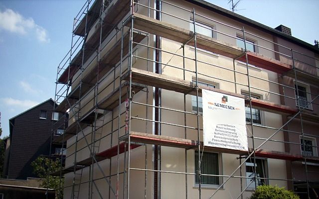Hausecke eines Mehrfamilienhauses mit Baugerüst und Bauschild