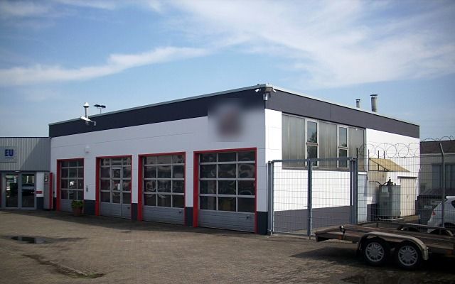 Werkstatthalle mit weißer Fassade, roten Rolltoren und dunklem Dachrand