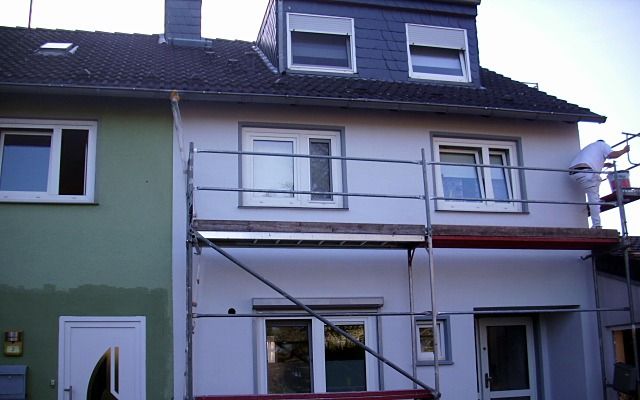 Reihenhaus mit frischem Anstrich in Grau- und Fliedertönen, ein Maler auf dem Gerüst