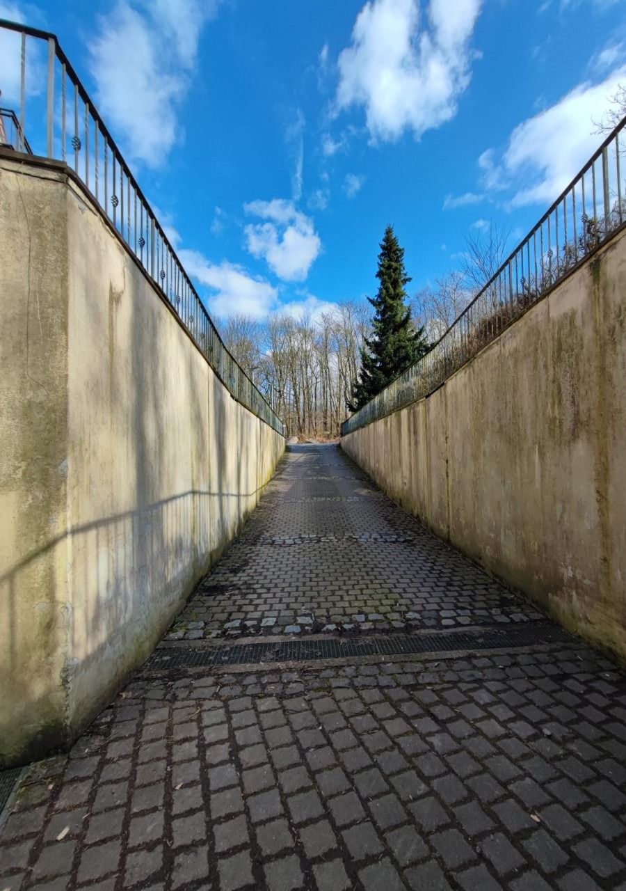 Gepflasterte Rampe zwischen zwei verschmutzten Betonstützwänden mit Geländer