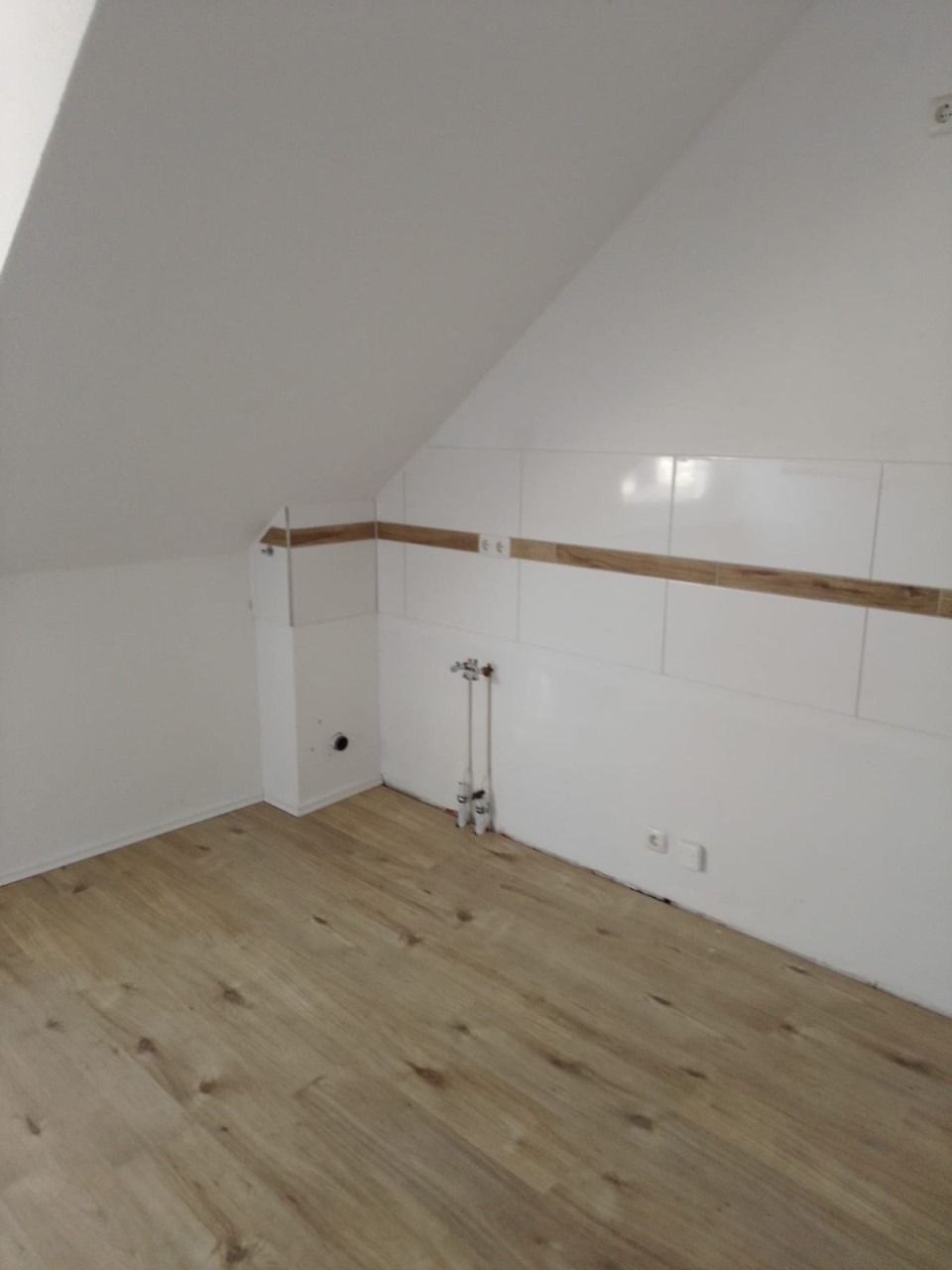 Raum mit Dachschräge, weißen Wänden, Fliesenspiegel und Boden in Holzoptik