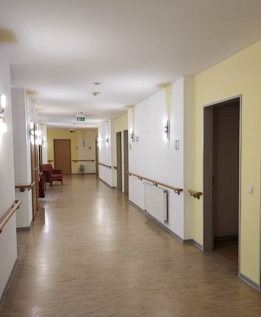 Langer Flur mit weißen und gelben Wänden und durchgehenden Handläufen