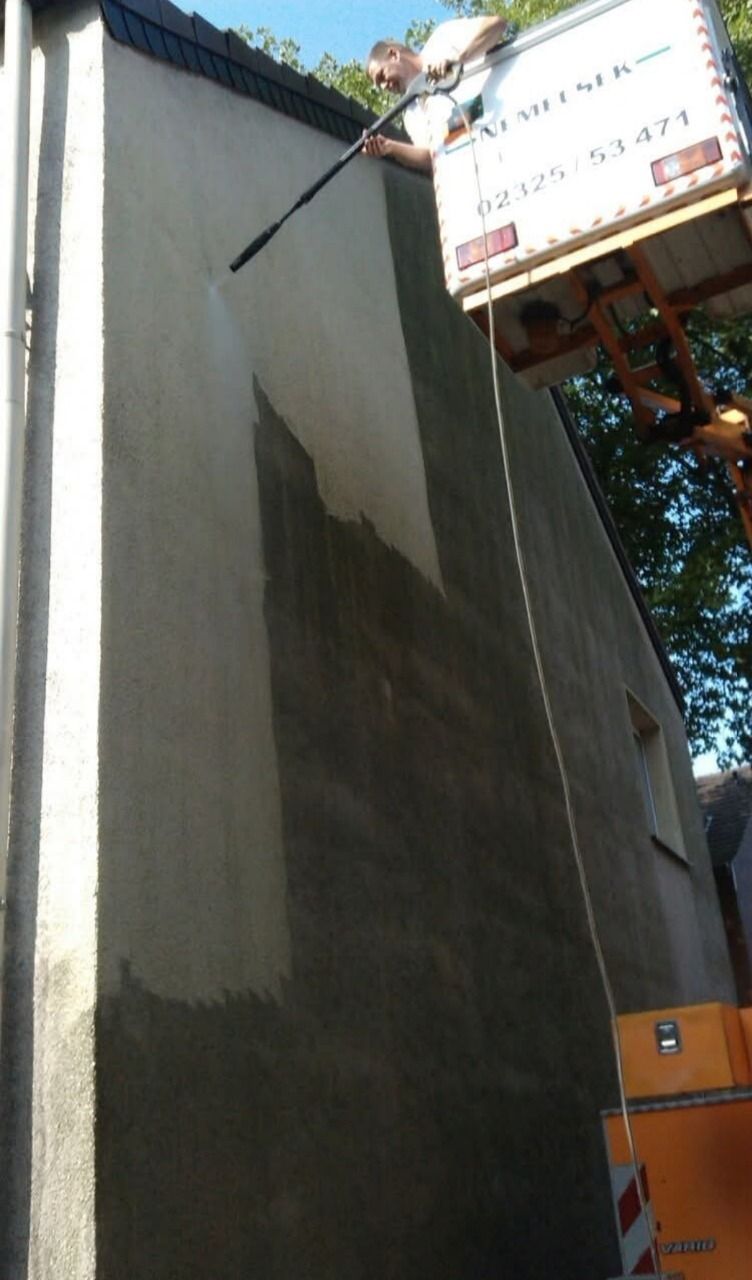 Hohe Hauswand, oben die Hubarbeitsbühne mit Nemecsek-Aufschrift, eine Hälfte der Wand bereits gereinigt